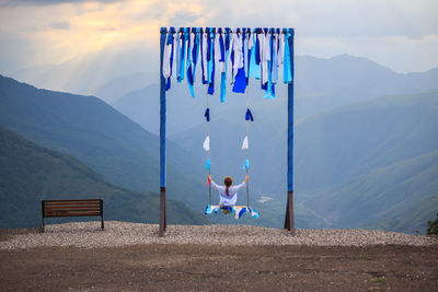 Rear view of woman sitting on bench against mountain