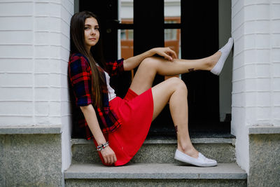 Full length portrait of beautiful woman sitting outside building