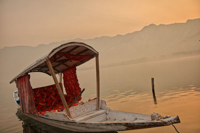 Boat on wooden post in lake against sky during sunset