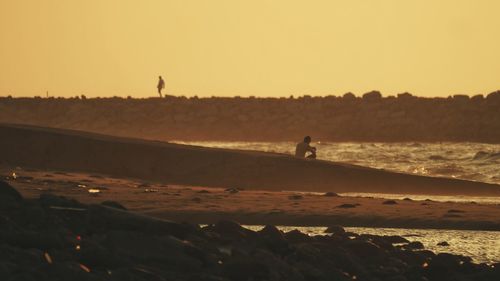 Silhouette man on beach against sky during sunset