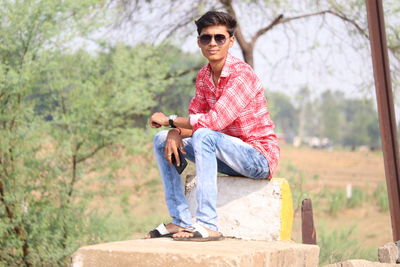 Portrait of young man sitting against trees