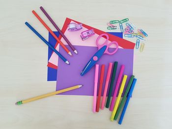 Directly above shot of multi colored papers with pens and scissors on table