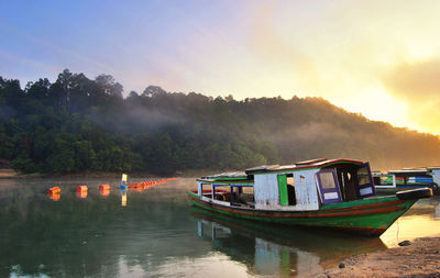 Boat moored in lake against sky during sunset