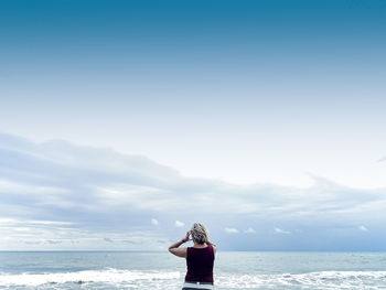 Rear view of woman standing on sea shore against sky