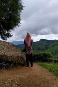 Rear view of woman standing on street amidst trees against sky