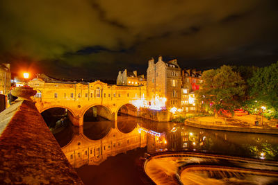 Illuminated bridge over road by city against sky at night