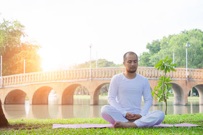 Portrait of young man sitting on bridge against sky