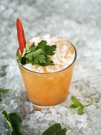 Close-up of drink garnish with bell pepper and herb in glass on crushed ice