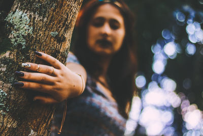 Low angle view of young woman touching tree trunk