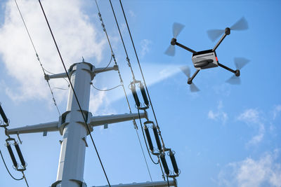 Low angle view of drone flying by electricity pylon against sky