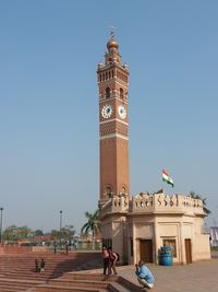 People in front of clock tower against blue sky
