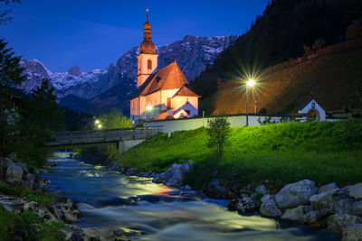 Illuminated buildings by trees against sky at night