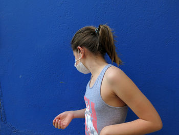 Woman looking away while standing against blue wall