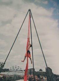 Low angle view of man doing gymnastics against cloudy sky