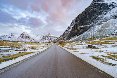 Empty road amidst snowcapped mountains against sky