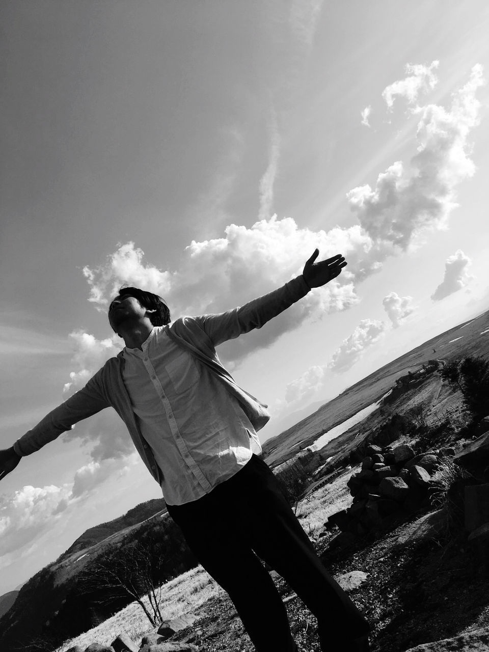 LOW ANGLE VIEW OF MAN WITH ARMS OUTSTRETCHED AGAINST MOUNTAIN