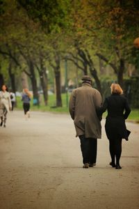 Rear view of couple holding hands while walking in park