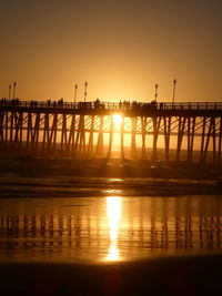 Silhouette pier on lake against orange sky