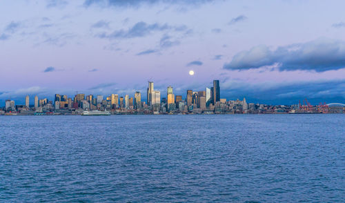 A full moon shines above the seattle skyline.