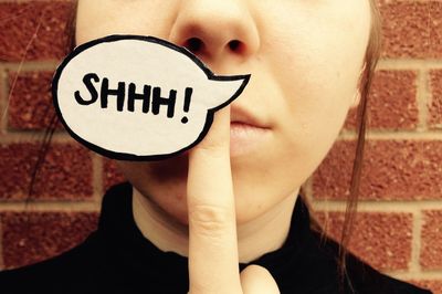 Cropped image of woman with text on speech bubble against brick wall