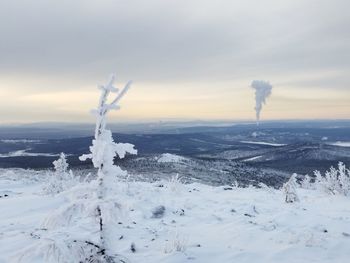 Smoke emitting from snow covered land against sky during sunset
