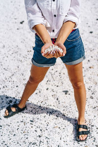 Low section of woman holding pebbles in heart shaped hands at beach