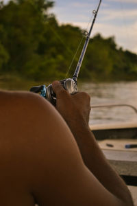 Midsection of person holding fishing rod against sky