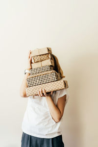 Young cheerful female holds a stack of gift boxes packed in craft paper and hides behind them.