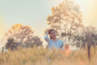 Young woman with guitar amidst plants on field against sky during sunset