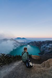 Man sitting on mountain against sky