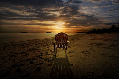 Deck chairs on beach against sky during sunset