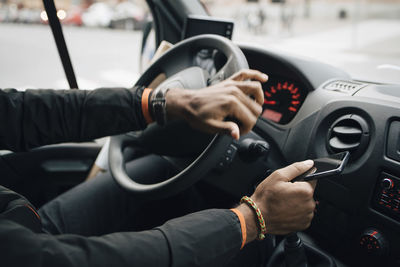 Cropped image of man holding mobile phone while driving delivery van