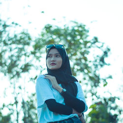 Portrait of young woman standing against trees