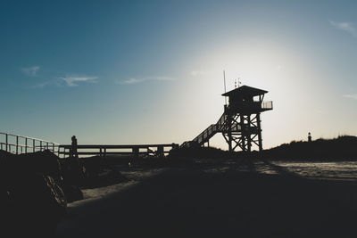 Silhouette bridge over sea against sky during sunset