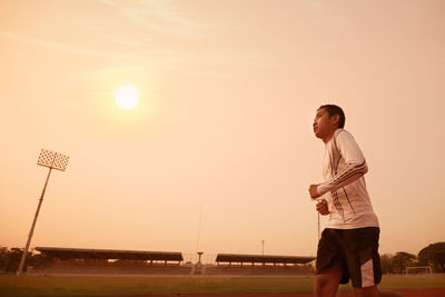 Teenage boy running on sports track against orange sky