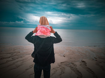 Rear view of woman standing on beach against sky