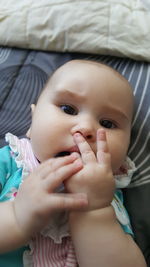 High angle portrait of baby girl sucking fingers while lying on bed