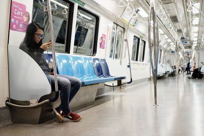 Full length of woman using mobile phone while sitting in subway train