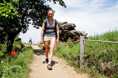 Portrait of smiling young woman hiking on trail against sky