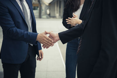 Businessmen shaking hands while standing by colleague in city
