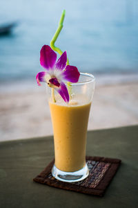 Close-up of mango smoothie with flower served on table at beach