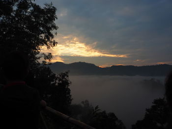 Rear view of girl by lake against sky during sunset