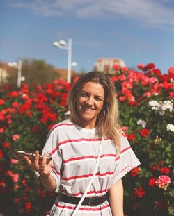 Portrait of a smiling young woman standing on red flowering plants