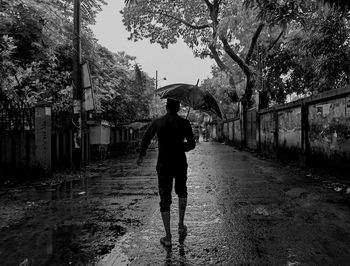 Full length of man walking on wet street during rainy season