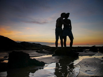 Silhouette friends standing at beach against sky during sunset