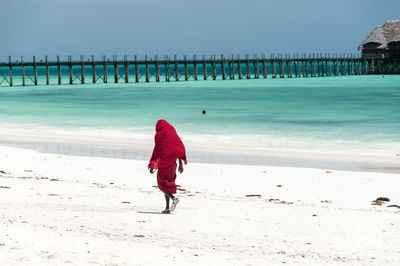 Rear view of masai warrior walking at beach against sky