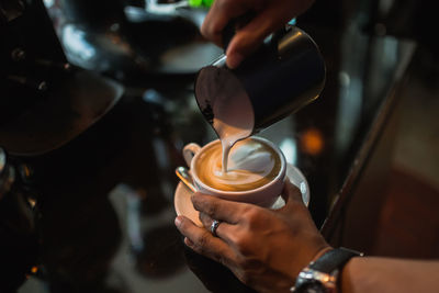 Cropped hands pouring milk in coffee