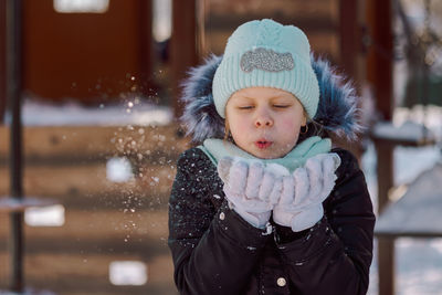 Little girl blows snow from her palms on a walk on a frosty winter day