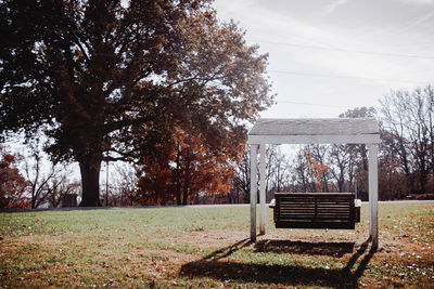 Empty bench on field by trees against sky