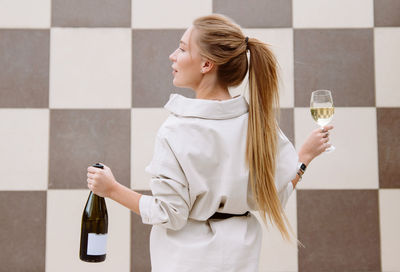 Young woman tasting white wine against chessboard background